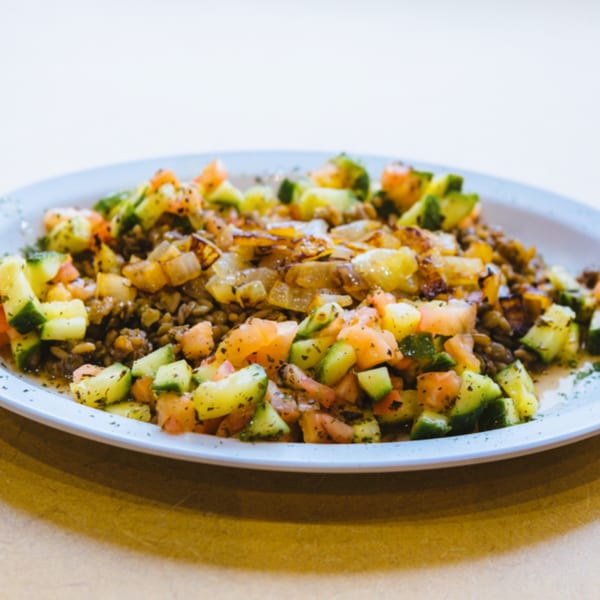 A close-up of a salad with diced cucumbers, tomatoes, and caramelized onions on a white plate.
