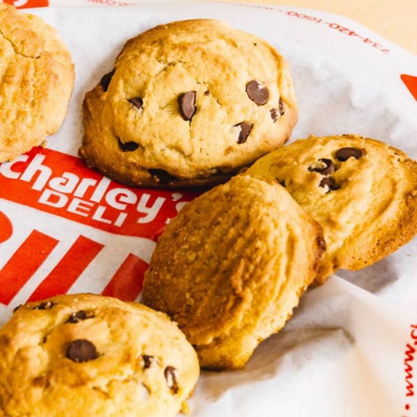 Several golden-brown chocolate chip cookies on white paper with the red "Charley's Deli" logo.