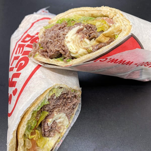 Two Charley's Deli and Grille cheesesteak sandwiches, wrapped in paper, filled with meat, cheese, and lettuce.
