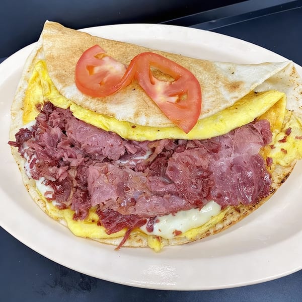 A Charley's Deli and Grille breakfast wrap with eggs, corned beef, cheese, and tomato slices.
