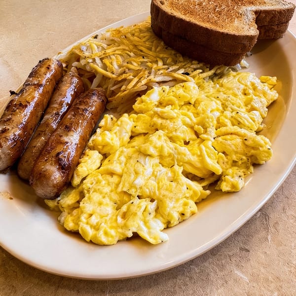 A breakfast plate with three sausages, scrambled eggs, hash browns, and two slices of toast.