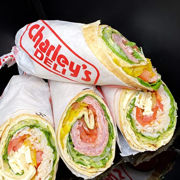 Three Charley's Deli wraps, one with the logo visible, filled with meats, cheeses, and vegetables.